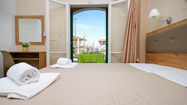 A hotel room with a bed, a green table, a mirror, and a view of the outside. - Stavros Apartments Gouvia Marina (Corfu)
