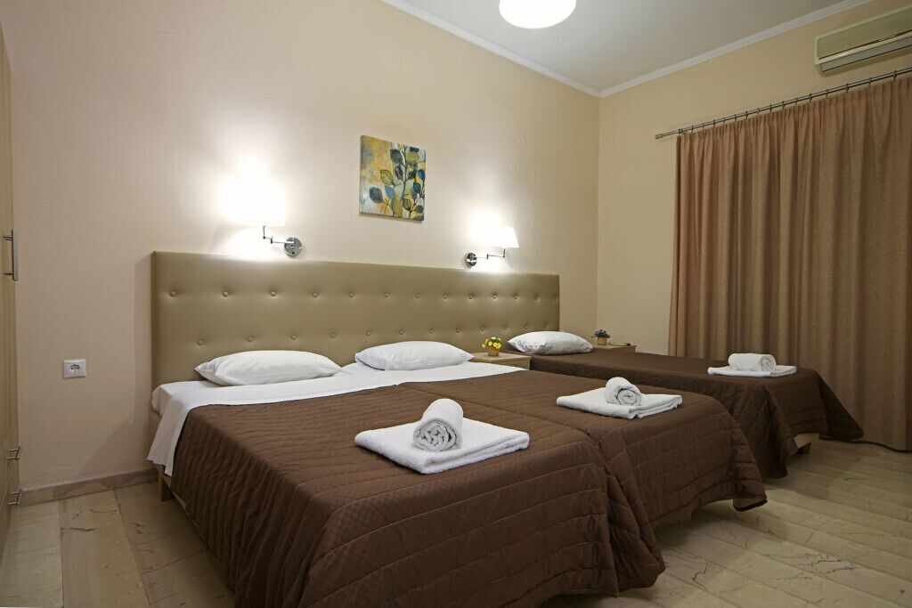 Una habitación de hotel con dos camas, paredes color beige, un cabecero grande y un cuadro.