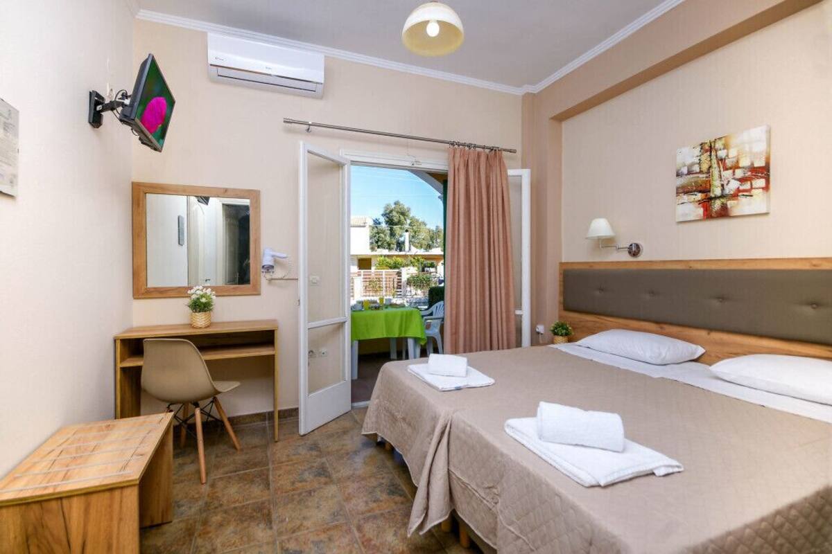 A hotel room with a bed, a desk, a chair, a mirror, and a view of the outside.