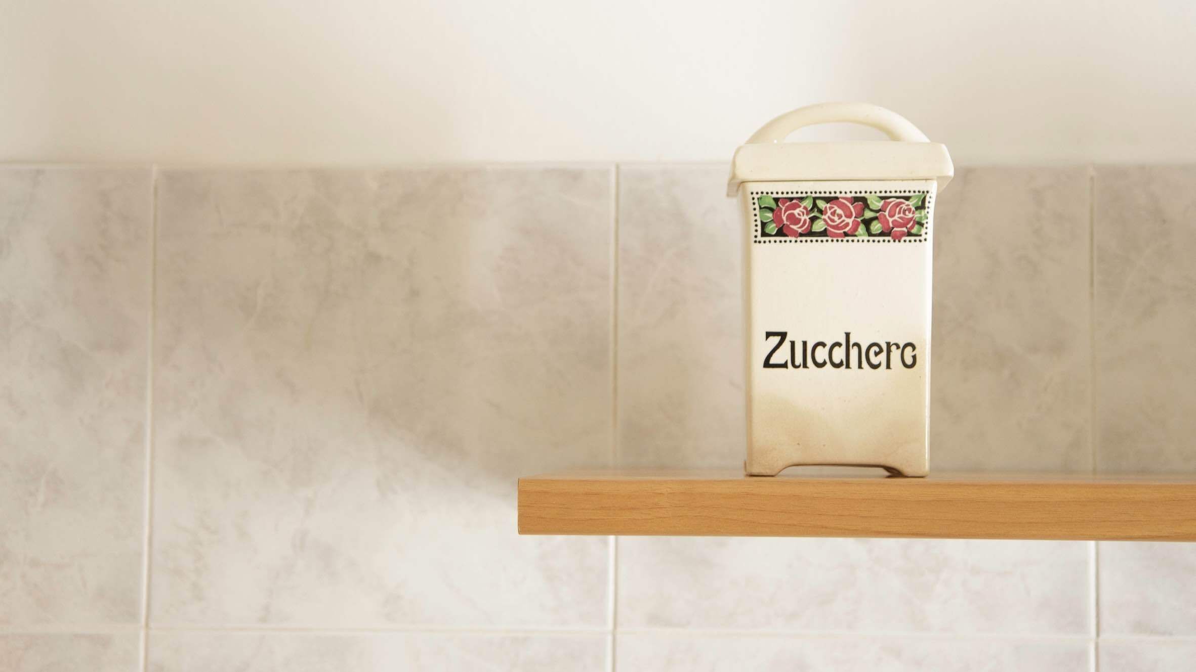 A kitchen with a shelf holding a white container labeled "Zucchero" with a handle.