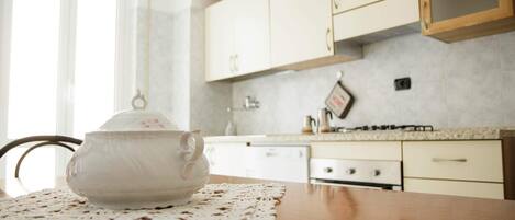 A kitchen with white cabinets, a stove, and a teapot on a table with a lace placemat.