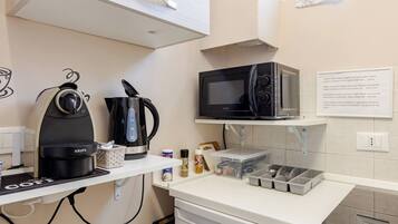 Eine Küchenzeile mit Kaffeemaschine, Wasserkocher, Mikrowelle und kleinem Kühlschrank.