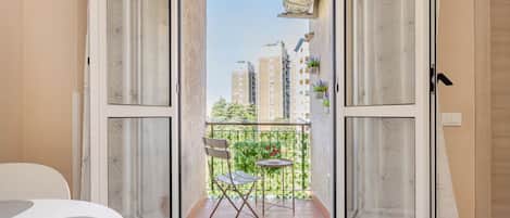 An open balcony with a chair, a small table, and a view of buildings in the distance.