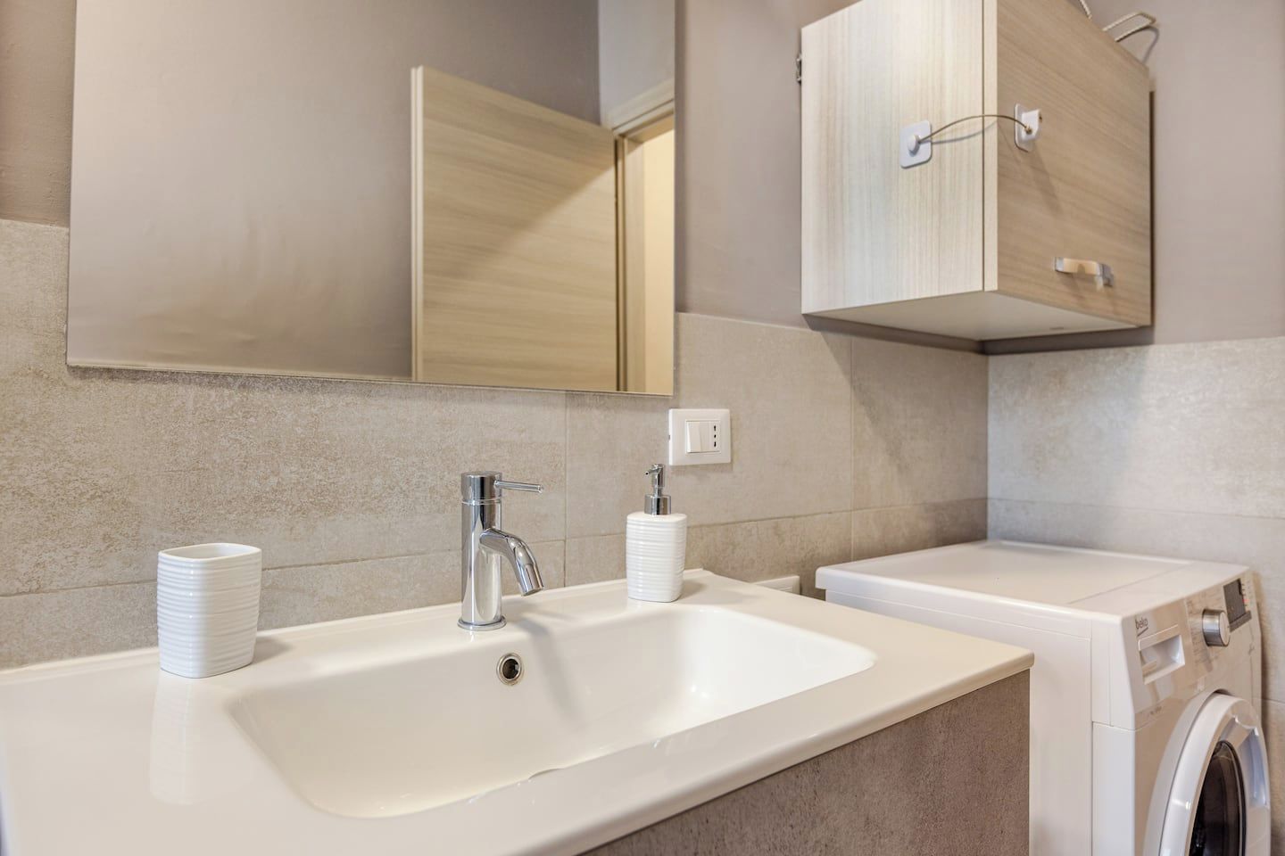 Une salle de bain moderne avec un lavabo blanc, un miroir et un lave-linge encastré.