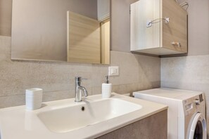 Une salle de bain moderne avec un lavabo blanc, un miroir et un lave-linge encastré.