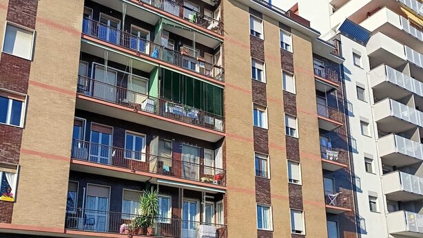 Un edificio residencial de varios pisos con balcones, entrada a nivel de la calle y puerta de garaje visible.
