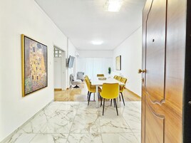 Uma sala de jantar com uma mesa branca, cadeiras amarelas e um quadro na parede.