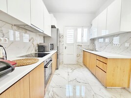 Cozinha moderna com armários brancos, painel de fundo de mármore e bancada de madeira.