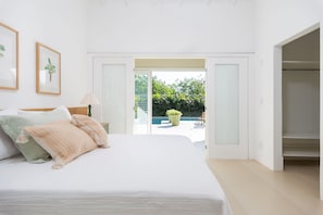 Un dormitorio con cama, mesita de noche, lámpara y vistas a una zona de piscina al aire libre.