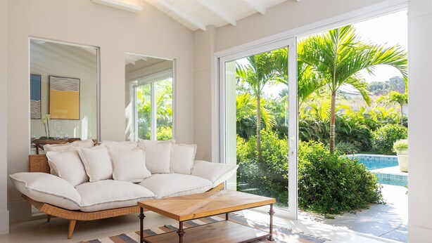 A modern living room with a white sofa, a wooden coffee table, and a large glass door leading to a pool area.
