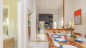 A modern dining area with a long table set for six, a kitchen in the background, and a bright, airy space with natural light.