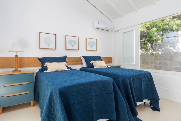 Une chambre avec deux lits, une table de chevet, une lampe et des œuvres d’art encadrées accrochées au mur.