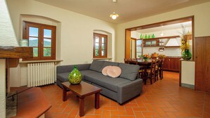 A living room with a grey sofa, wooden coffee table, and a dining area with a wooden table and chairs. - the farmhouse. (Vinci)
