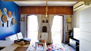 Una habitación con una cama, una mesa con bandeja, una silla, un televisor y un tapete geométrico de colores.