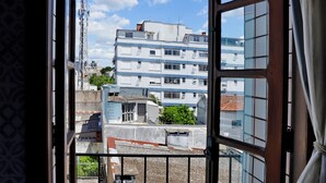 Un balcón con vista a un edificio de varios pisos y un cielo azul despejado.