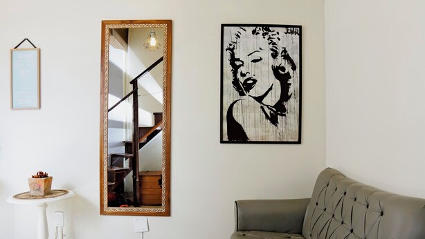 Una sala de estar con un sofá gris, un tapete redondo tejido, un espejo y una obra de arte blanco y negro en la pared.