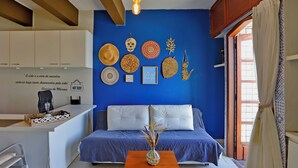 Un espacio de sala acogedor con pared azul, un sofá, una mesa de centro y una zona de cocina con mostrador y armarios.