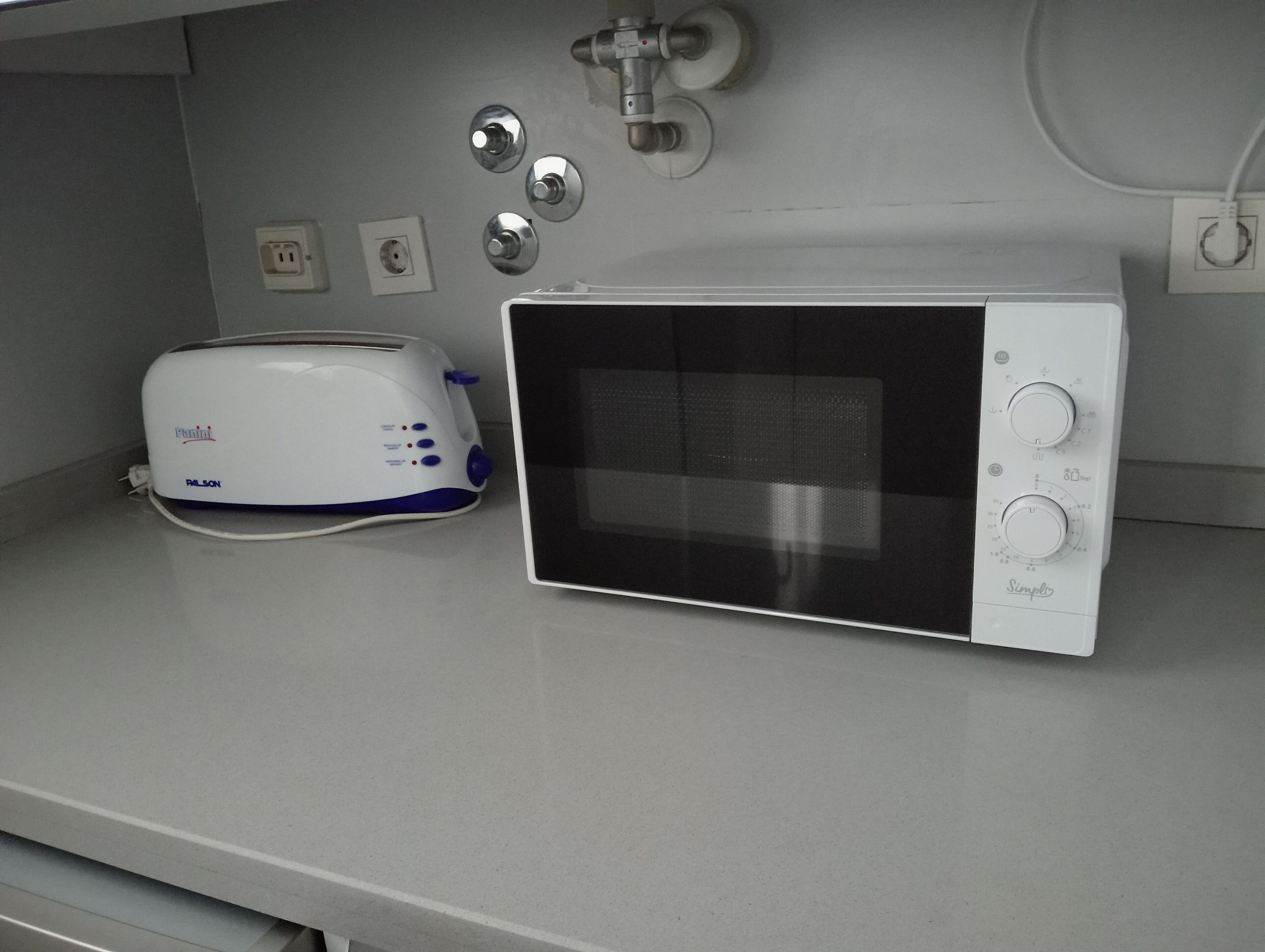 Een kitchenette met een witte toaster, een magnetron en een spoelbak met een kraan.