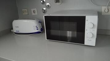 Een kitchenette met een witte toaster, een magnetron en een spoelbak met een kraan.