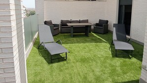 Une terrasse extérieure avec une table et des chaises, entourée de gazon synthétique, et un mur en briques blanches.
