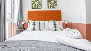 A hotel room with a bed, two pillows, a headboard, and two wall-mounted artworks.