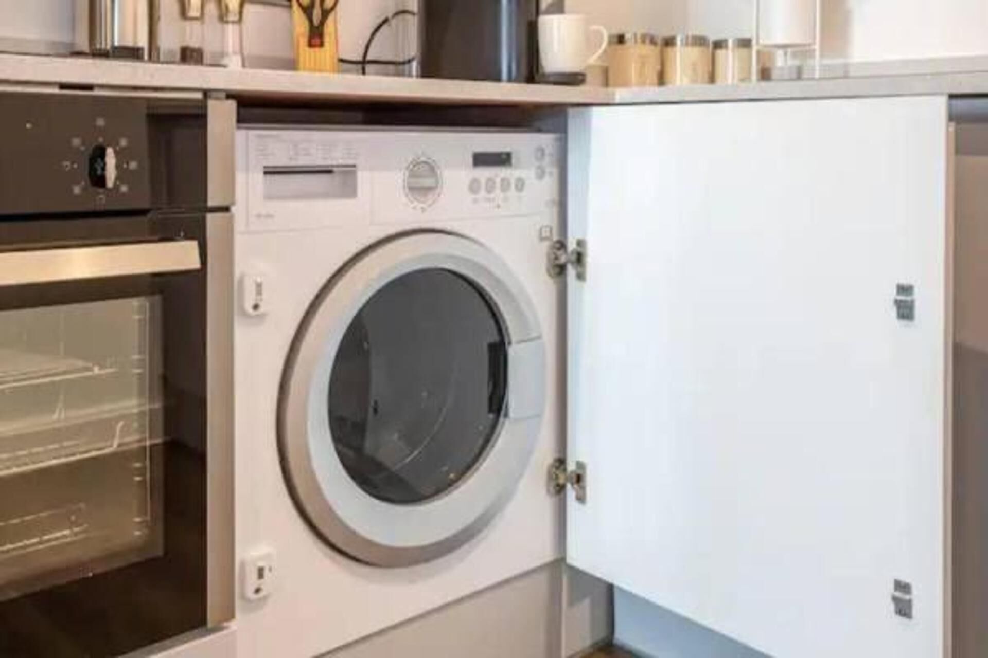 A compact, modern laundry room with a front-loading washing machine and a built-in oven.