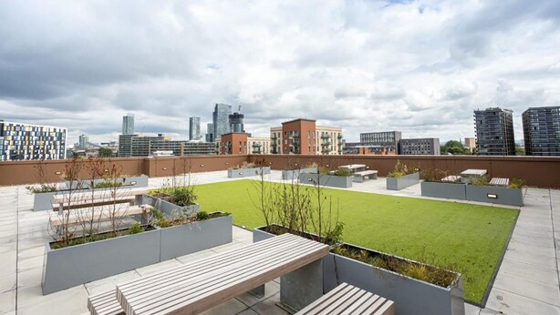 A rooftop terrace with a green lawn, seating areas, and a city skyline in the background.