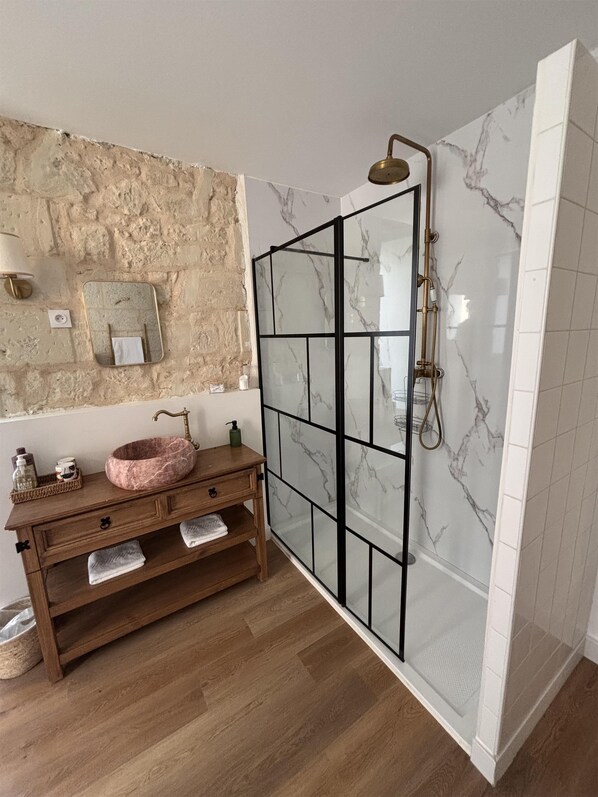 A bathroom with a marble shower, wooden vanity, and a stone wall.