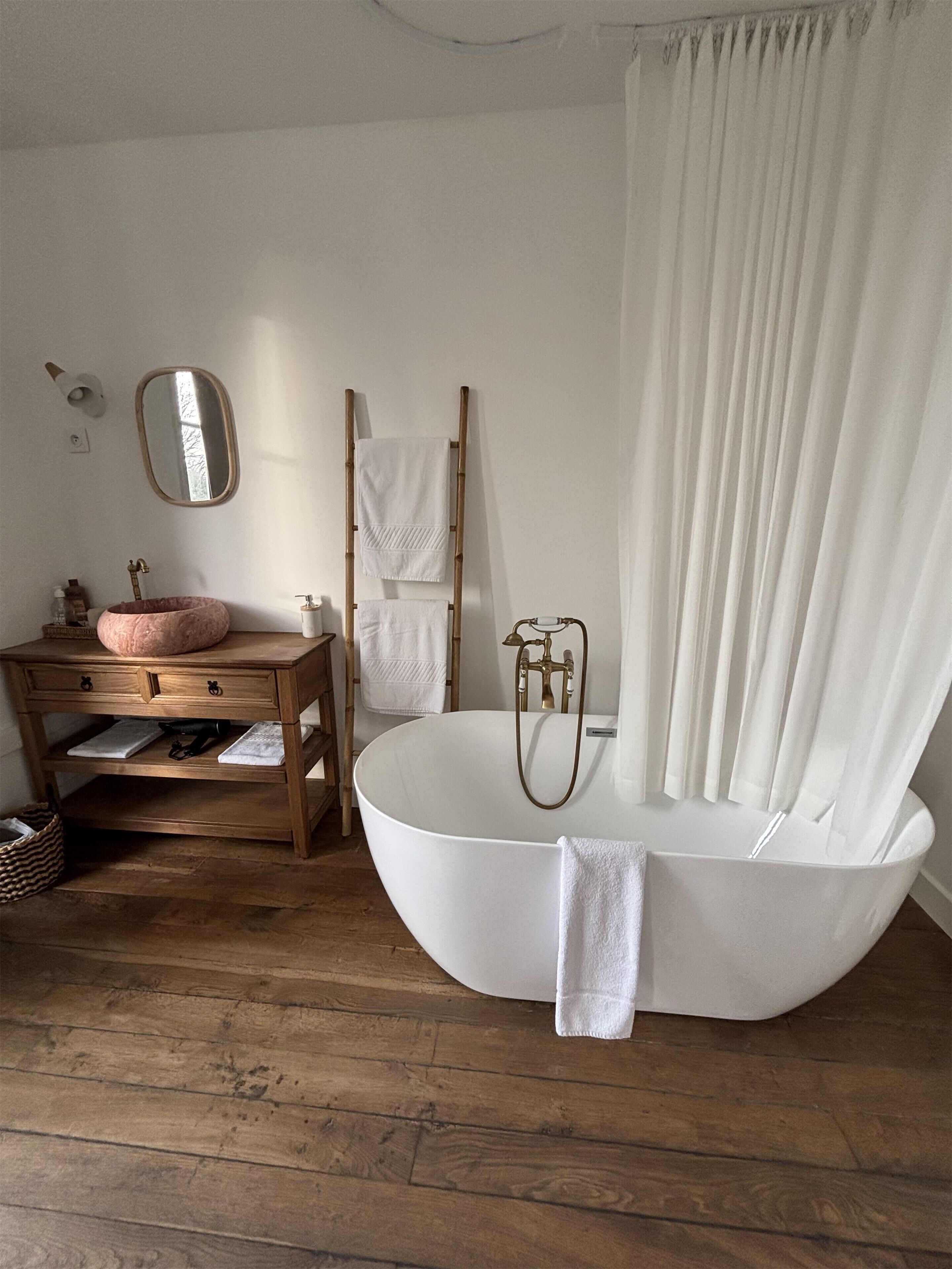 A bathroom with a freestanding bathtub, a wooden vanity, a mirror, and a towel rack.