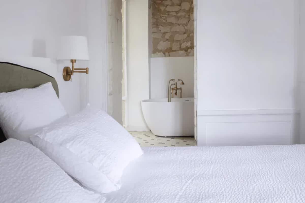 Une chambre avec un lit, une salle de bain avec une baignoire et un mur en pierre.