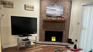 A living room with a flat-screen TV, a brick fireplace, and a mounted TV above it. - Home away from home (Conway)