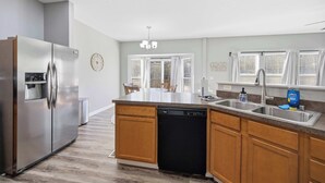 A modern kitchen with a stainless steel refrigerator, wooden cabinets, a dishwasher, and a large island with a sink. - Ark & Creation Retreat For 12! (Walton)
