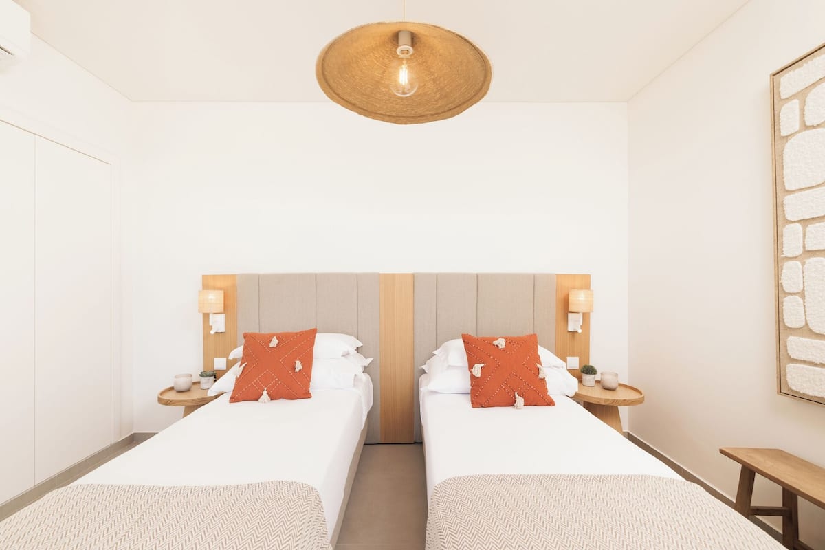 A hotel room with two beds, a wooden headboard, bedside lamps, and a hanging light fixture.