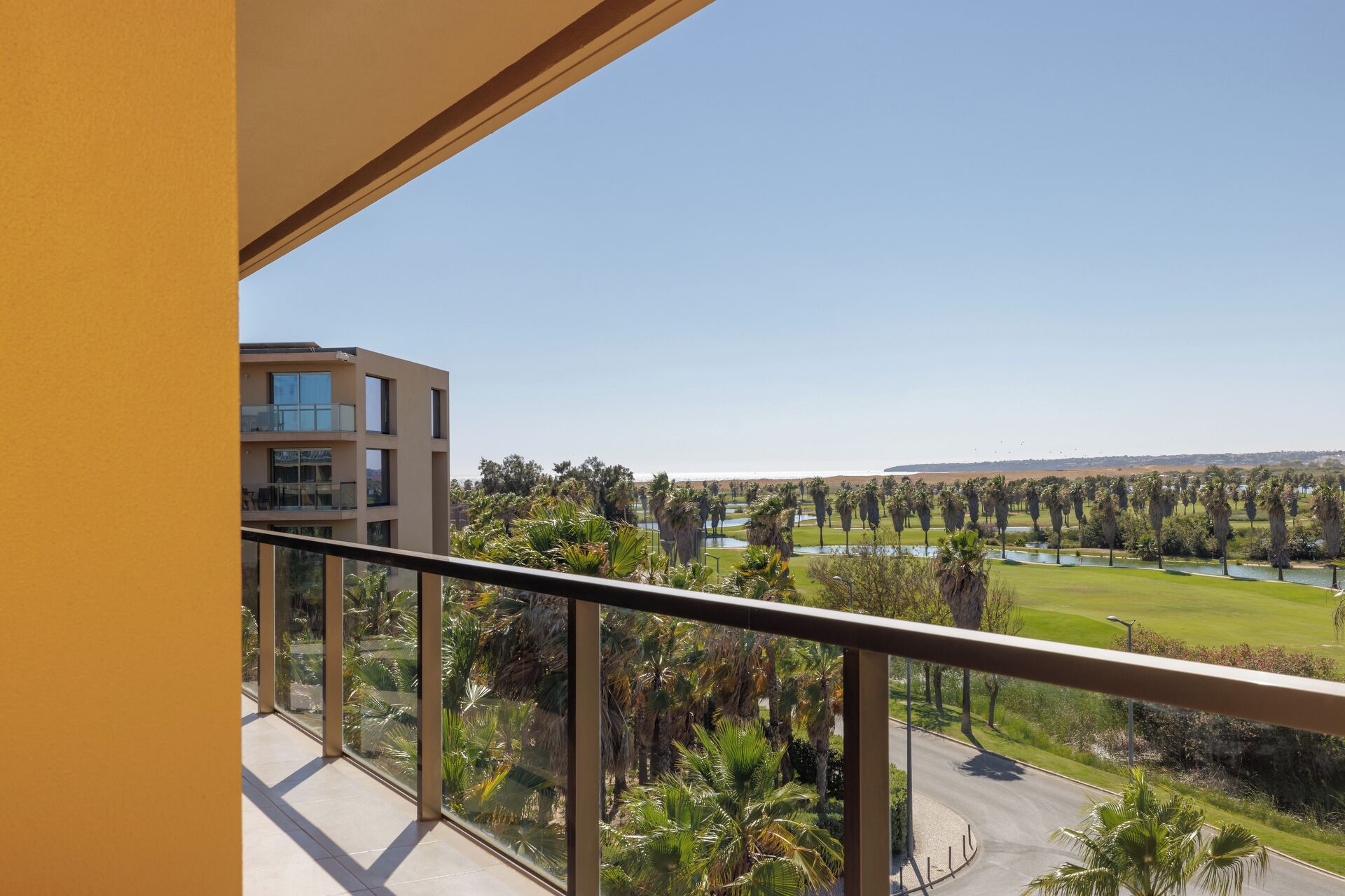 A balcony with a view of a modern building, a golf course, and a clear sky.