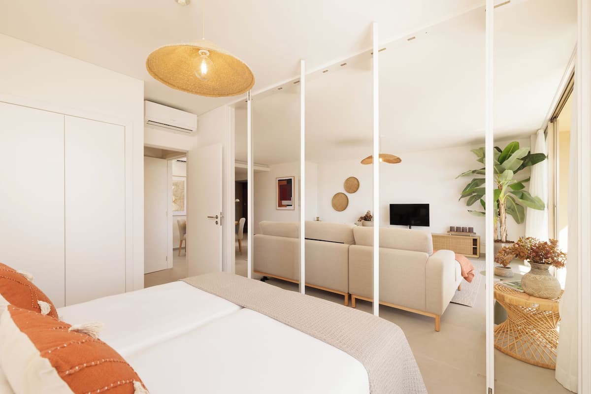 A modern bedroom with a bed, a sofa, a TV, and a large plant.