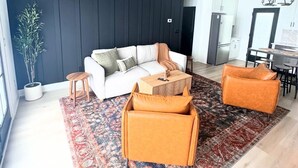 A modern living room with a white sofa, a patterned rug, and a dining area with a chandelier. - The Adelyn, where comfort meets convenience (Jeffersonville)
