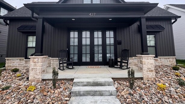 A modern two-story house with a dark exterior, a covered front porch with stone pillars, and a stone pathway leading to the entrance. - The Adelyn, where comfort meets convenience (Jeffersonville)