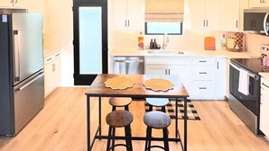 A modern kitchen with white cabinets, a central island with stools, a chandelier, and a refrigerator. - The Adelyn, where comfort meets convenience (Jeffersonville)