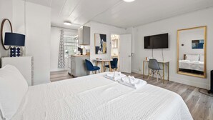 A hotel room with a large bed, a desk, two chairs, a TV, and a mirror. - Chic City Retreat 93F (Columbus)