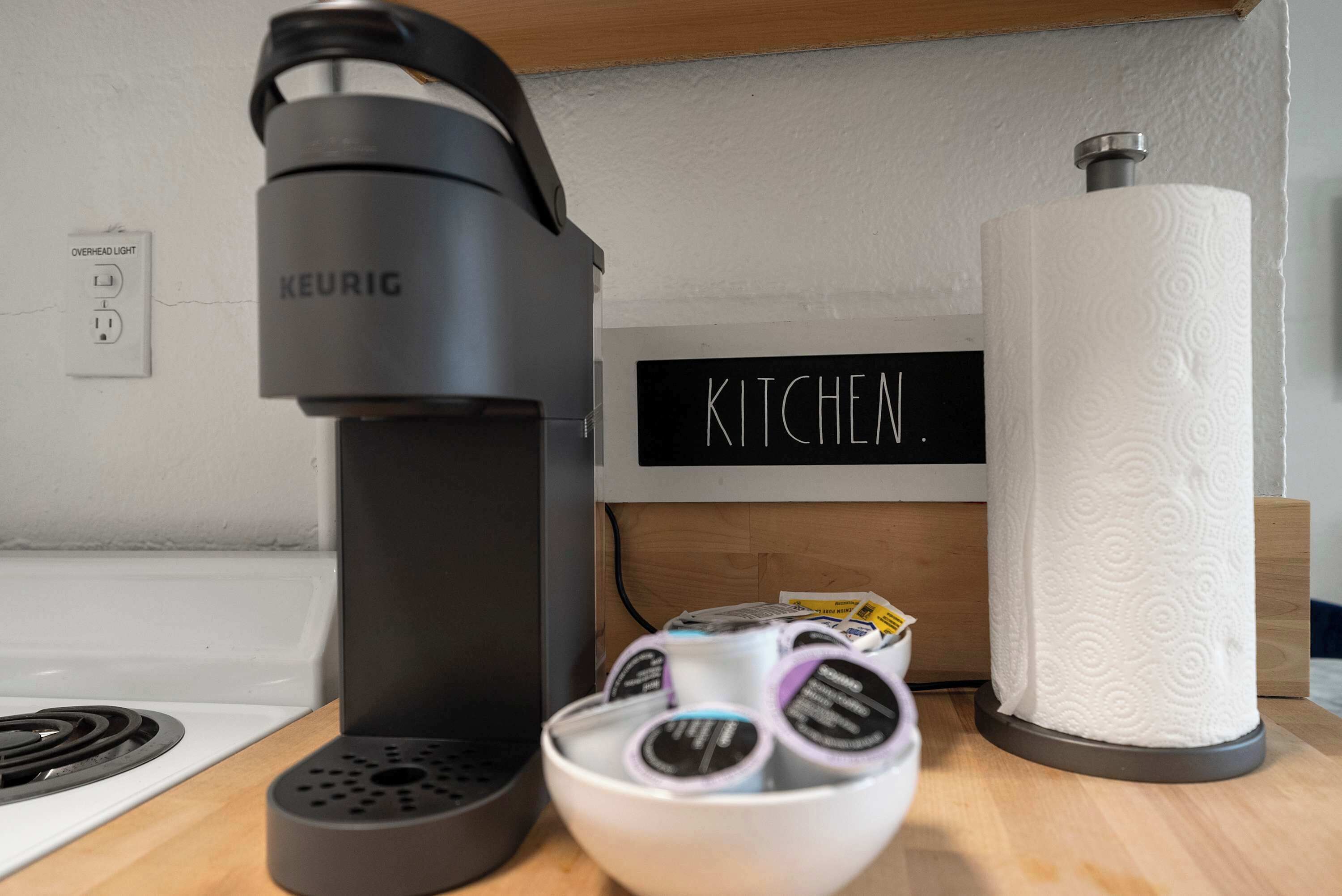 Un coin cuisine équipé d’une machine à café Keurig, d’un récipient rempli de dosettes de café et d’un rouleau d’essuie-tout.