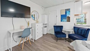 Una habitación moderna con un escritorio blanco, sillas azules, un televisor de pantalla plana, un espejo y un cuadro en la pared.
