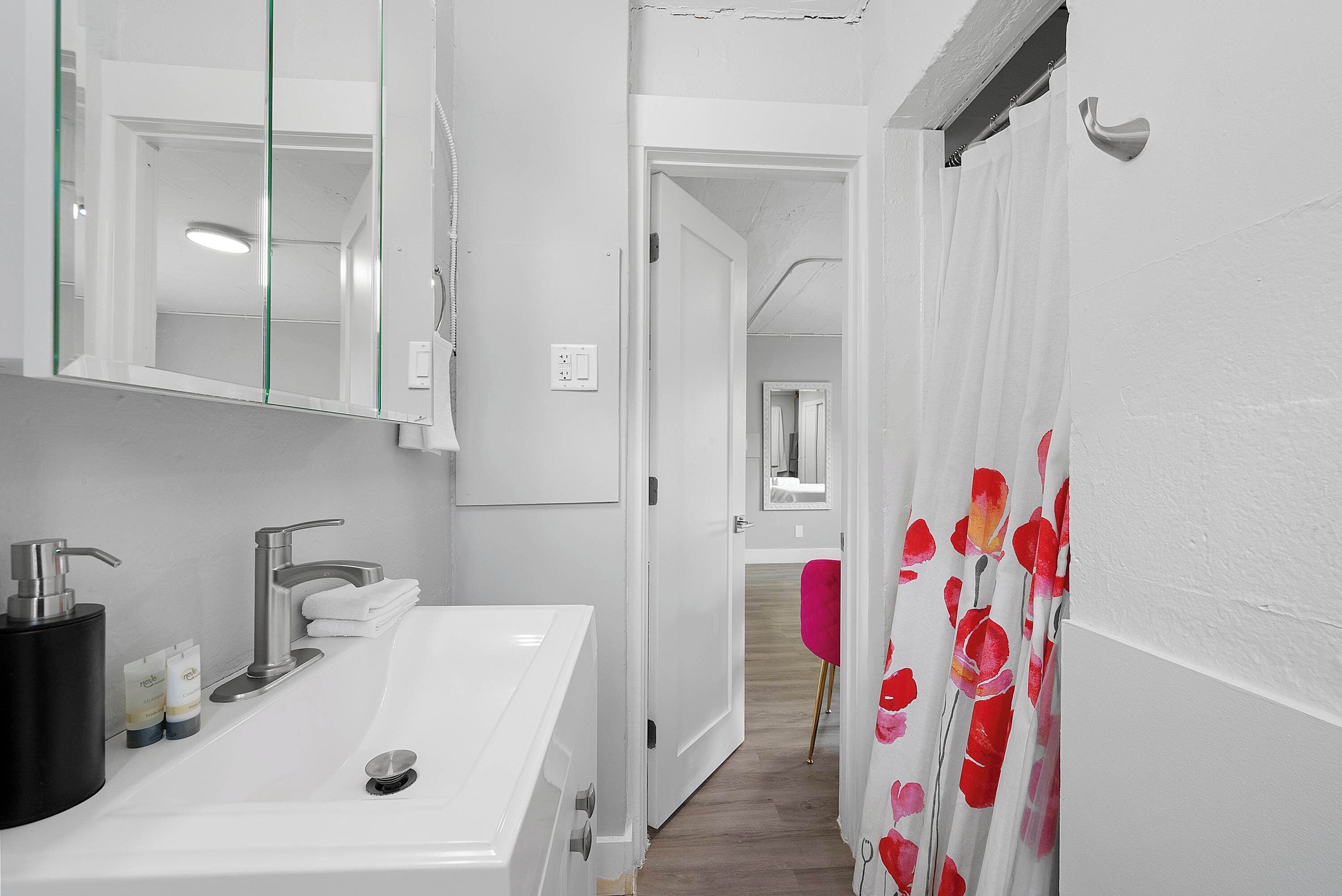 Une salle de bain avec un lavabo blanc, un miroir et un rideau de douche à motifs floraux.