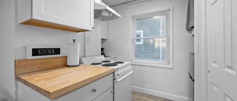 A compact kitchen with white cabinets, a wooden countertop, a stove, and a window with blinds.