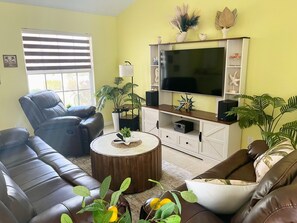 Ein Wohnzimmer mit einem großen Flachbildfernseher, Ledersofas, einem Couchtisch und Topfpflanzen.