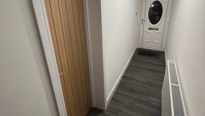 A hallway with a wooden door, a white wall, a vent, and a ceiling light. - Shawforth - 2 Beds - Sleeps 4 - Street Parking (Rochdale)