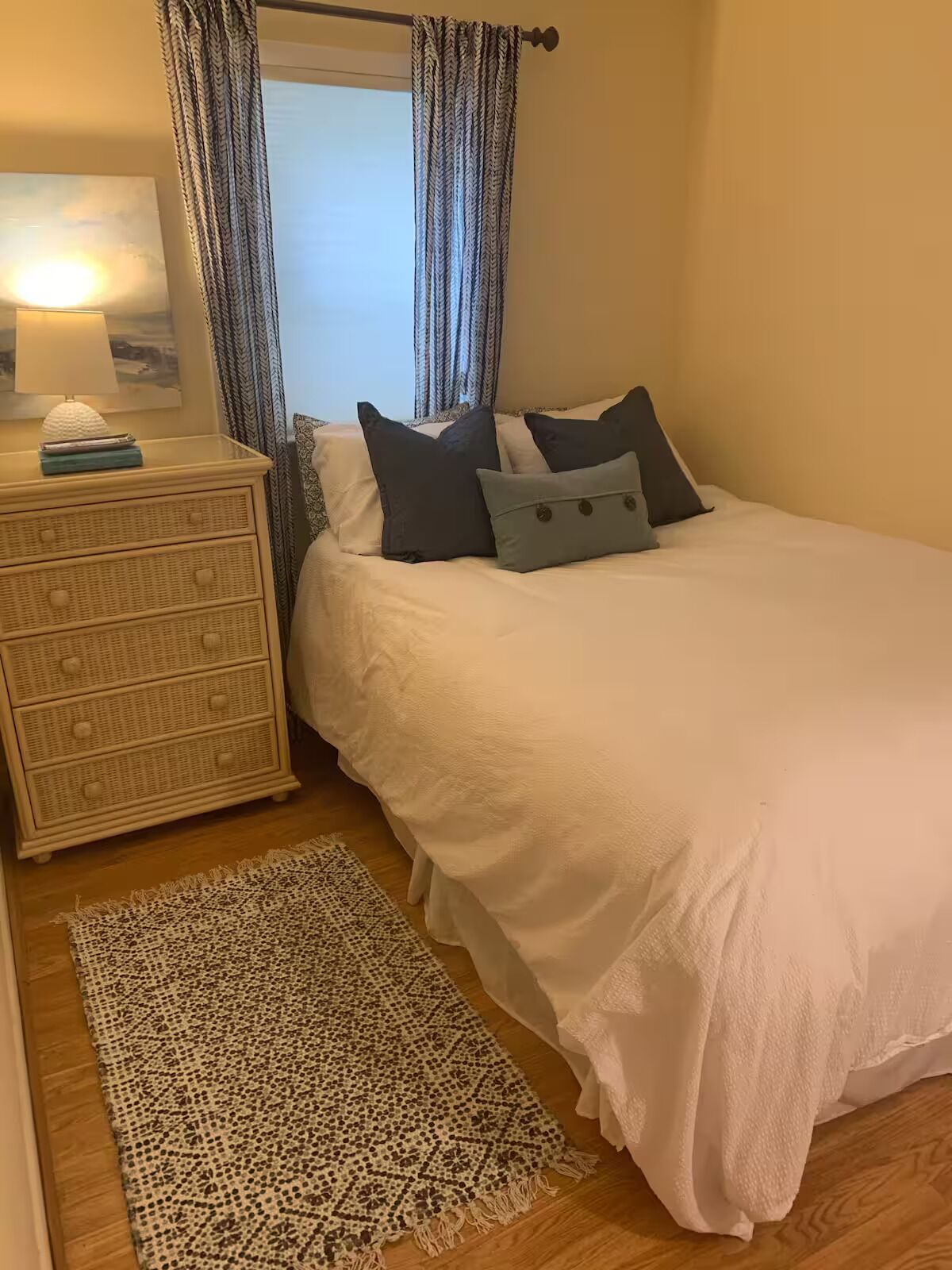 A bedroom with a bed, bedside table, lamp, and a patterned rug.