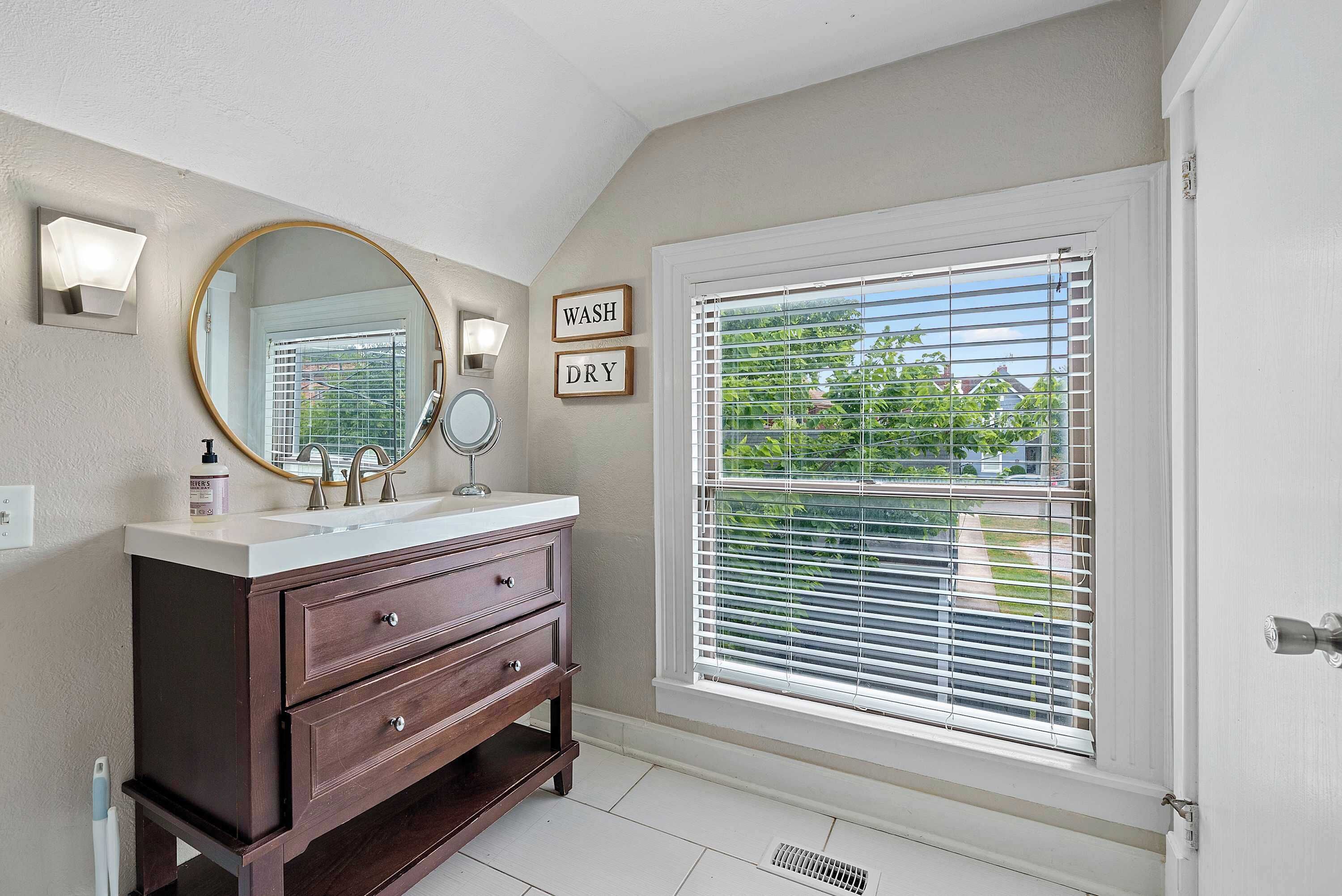 A bathroom with a vanity, a mirror, a sink, and a window with blinds.