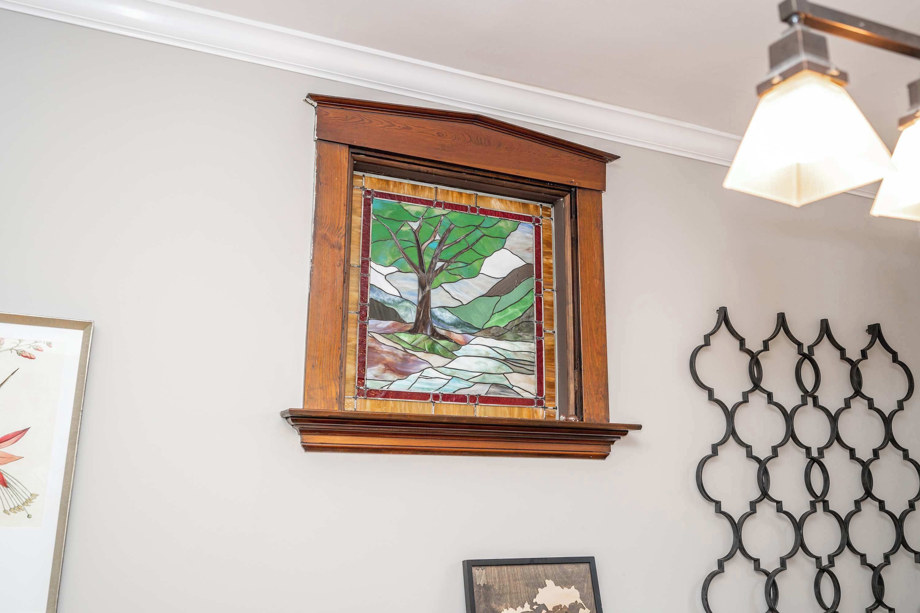 A stained glass window with a tree design, a framed picture to the left, and a decorative metal wall piece.