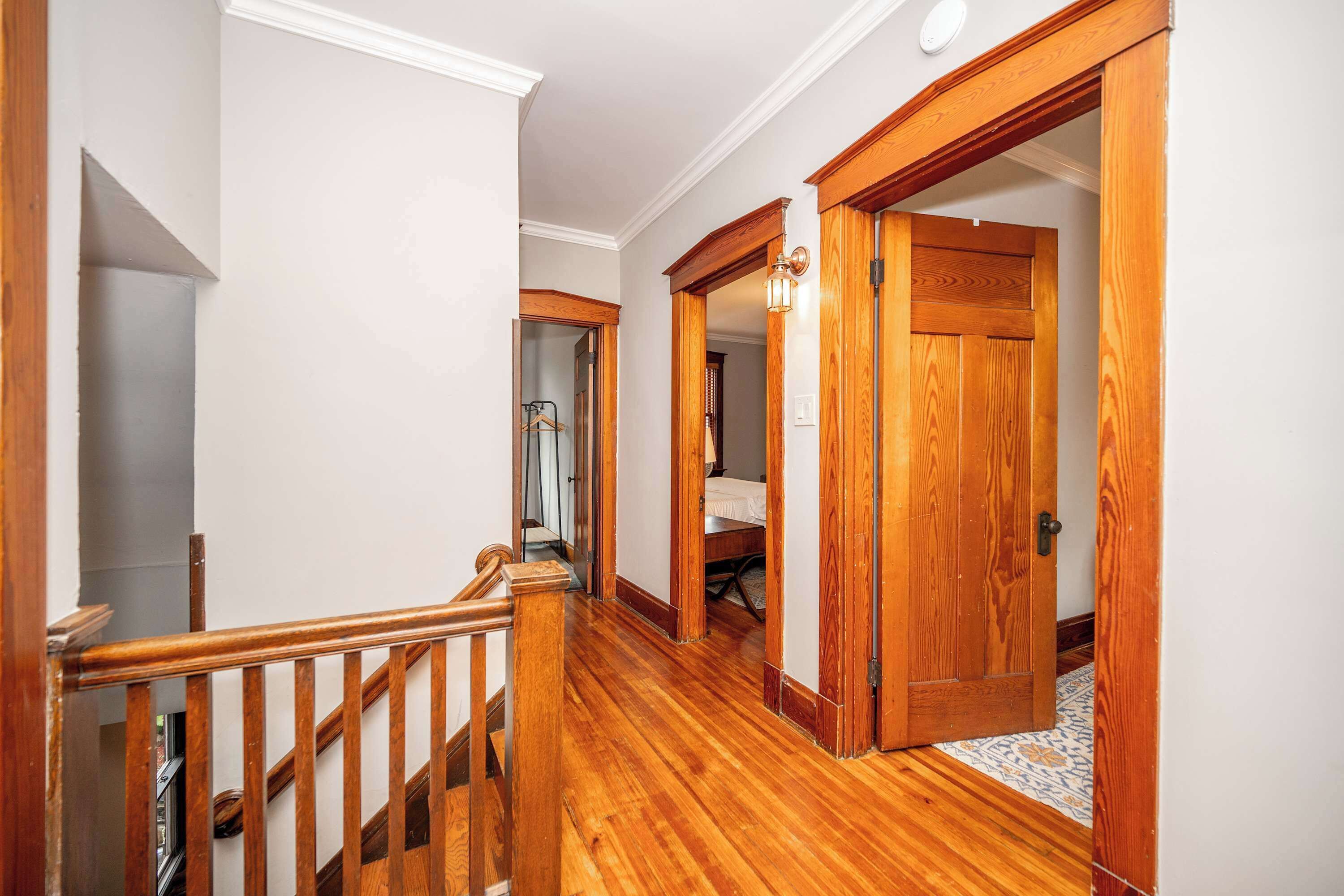 Un couloir doté d’un plancher en bois, d’un escalier en bois et d’une porte donnant sur une chambre.