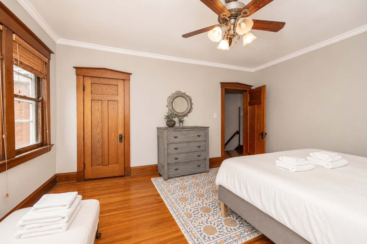 A bedroom with a bed, a dresser, a mirror, a ceiling fan, and a door leading to another room.